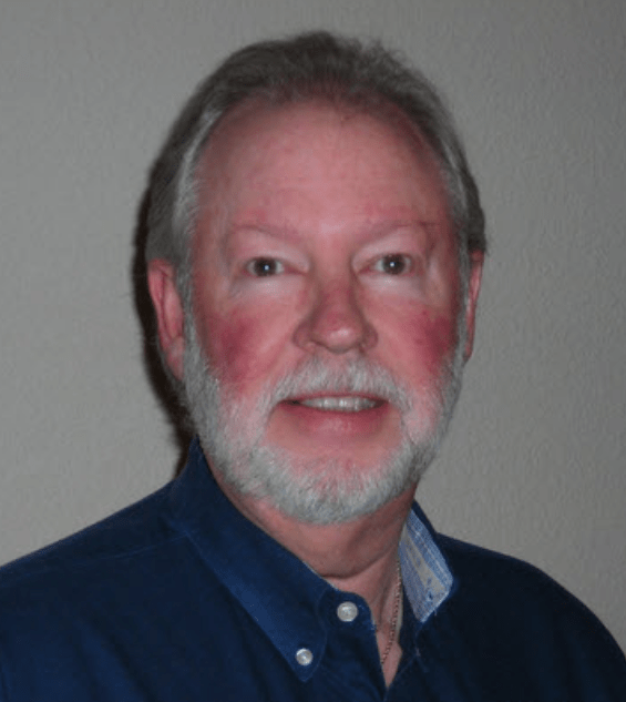 Man with short gray hair and a beard smiles at the camera